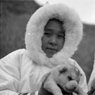 Photograph of two Inuit girls in white parkas holding puppies, unknown location, Nunavut, July 1951