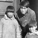 Photograph of an Inuit man and two children standing in a doorway, unknown location, Nunavut, no date